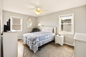 A bedroom with a bed, nightstands, a desk, a chair, a ceiling fan, and a window.