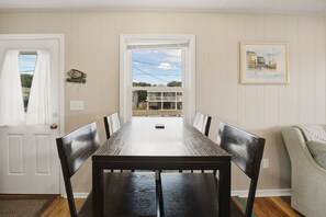 A dining room with a long table and chairs, a door with curtains, a wall clock, and a framed picture. - High Five: Classic OBX Escape Near the Beach (Kill Devil Hills)