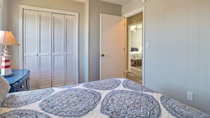 A bedroom with a bed, a nightstand, a lamp, a closet, and a door leading to another room. - High Five: Classic OBX Escape Near the Beach (Kill Devil Hills)