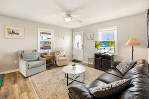 A living room with a sofa, armchair, coffee table, TV, and a ceiling fan. - High Five: Classic OBX Escape Near the Beach (Kill Devil Hills)