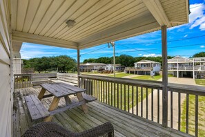 A covered porch with a picnic table and wicker chairs, overlooking a residential area with houses and a clear sky. - High Five: Classic OBX Escape Near the Beach (Kill Devil Hills)