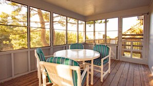 Un patio couvert avec une table ronde et des chaises, de grandes fenêtres et une terrasse en bois.