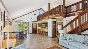 Un vaste espace de vie doté d’un haut plafond, d’un escalier en bois et offrant une vue sur l’extérieur.