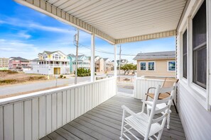 A covered porch with white railings and a wooden floor, overlooking a residential area with houses and a road. - 5200 Seaside * 5 Min Walk to Beach (Kill Devil Hills)