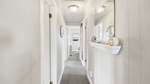 Um corredor com paredes brancas, carpete cinza e uma lareira de mármore branca adornada com objetos decorativos.