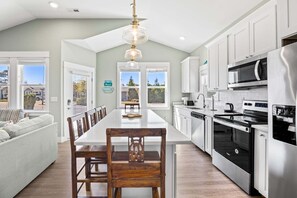 A modern kitchen with white cabinets, stainless steel appliances, and a long dining table.
