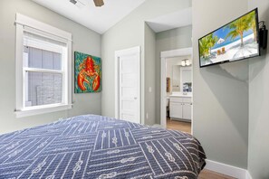 A bedroom with a bed, a painting, a TV, and a bathroom visible through an open door.