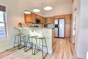 Une cuisine moderne avec des meubles en bois, un réfrigérateur en acier inoxydable, un four à micro-ondes et un coin bar avec des tabourets.