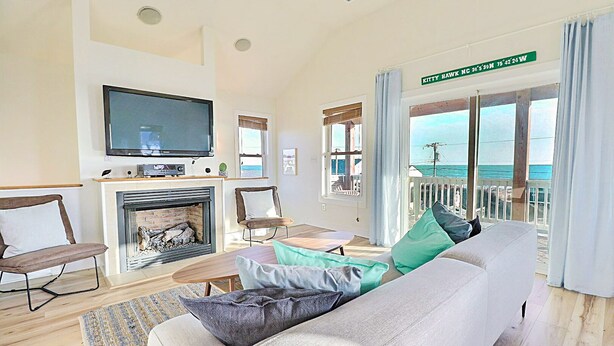 A spacious living room with a fireplace, a television, and a balcony with a view of the ocean. - The Shake Shack: Dog-Friendly + 450ft to Beach (Kitty Hawk)