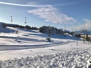 A snow-covered ski slope with ski lifts, trees, and a clear sky.