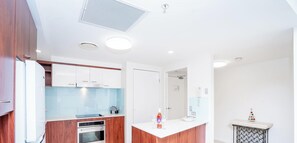 Une cuisine moderne avec des meubles blancs, un four encastré, un îlot central doté d’une plaque de cuisson en verre et un petit sapin de Noël décoratif.