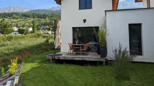 Ein modernes Haus mit einer Terrasse, einem Essbereich und Blick auf Berge.