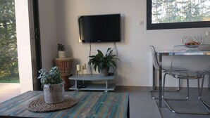 Ein modernes Wohnzimmer mit einem an der Wand montierten Fernseher, einem Esstisch mit Stühlen und verschiedenen Zimmerpflanzen.