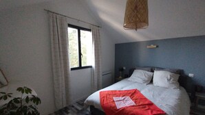 Ein Schlafzimmer mit Bett, Fenster, Pendelleuchte und Pflanze.