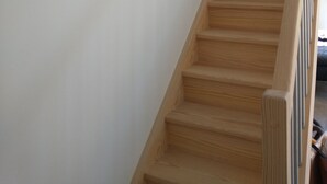 Eine HolztTreppe mit Handlauf, eine weiße Wand und eine dunkle Holzmaske auf der linken Seite.