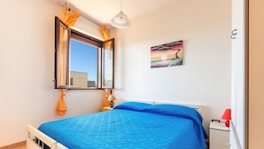 Un dormitorio con cama, mesita de noche, lámpara, un cuadro y una ventana con cortinas.