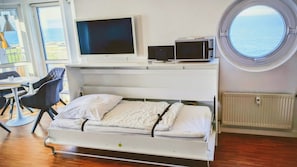 Una habitación con cama, escritorio y silla, televisor y ventana con vista al mar.