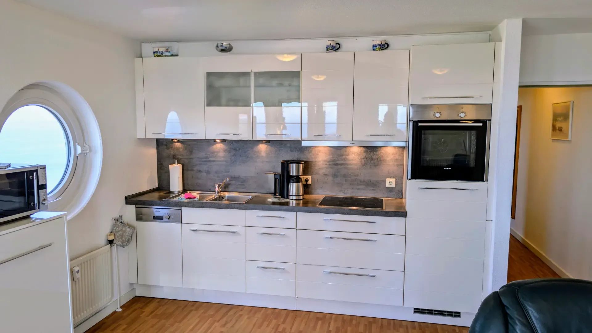 Una cocina compacta con gabinetes blancos, horno empotrado y ventana.