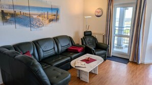 Una sala de estar con un sofá de cuero negro, un sillón a juego, una mesita de centro y un cuadro con una escena de playa.
