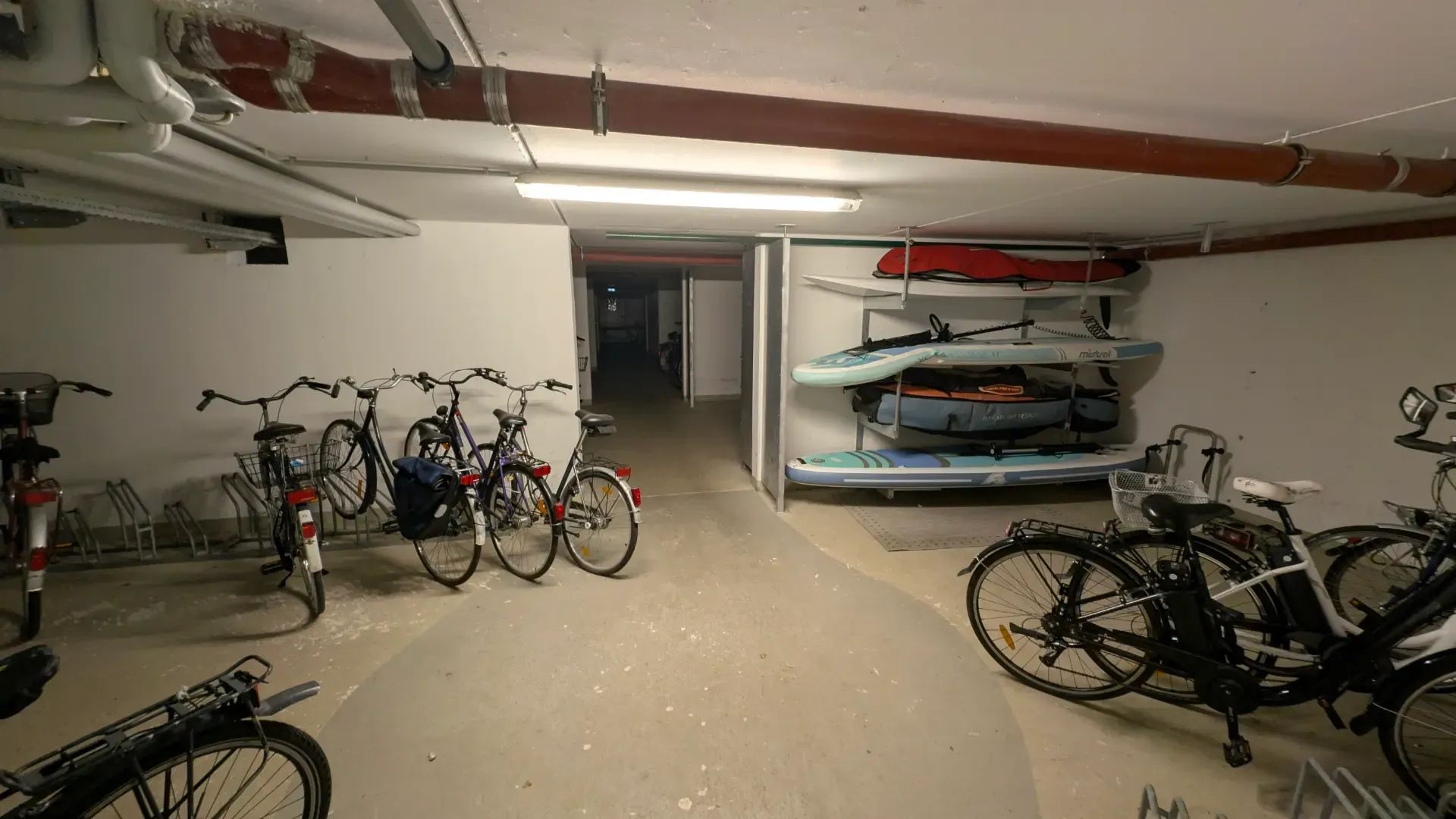 A bicycle storage area with multiple bicycles parked, a rack for kayaks, and a concrete floor.