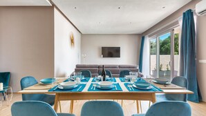 A dining area with a wooden table set for four, blue chairs, and a sofa in the background. - 2055 Villa San Teodoro (Avetrana)