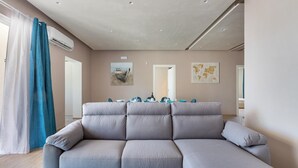 A modern living room with a grey sectional sofa, a dining table with chairs, and artwork on the walls. - 2055 Villa San Teodoro (Avetrana)
