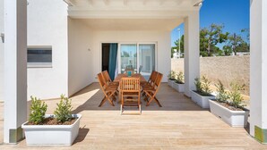 A covered patio with a wooden table and chairs, surrounded by white planters with small trees. - 2055 Villa San Teodoro (Avetrana)
