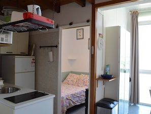A compact kitchen with a built-in stove, a small refrigerator, and a hanging rack above the sink.
