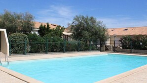 A rectangular swimming pool with a tiled edge, surrounded by a green fence, and a clear blue sky in the background.