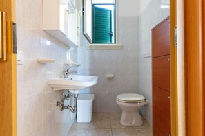 A compact bathroom with a sink, toilet, and a window with green shutters.