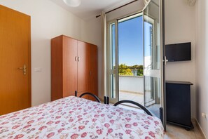 A bedroom with a bed, a wardrobe, a television, and a sliding glass door leading to a balcony.