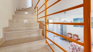 En trappa med beige marmortrappsteg och orangea handledare leder upp till en matplats med trästolar och ett bord.