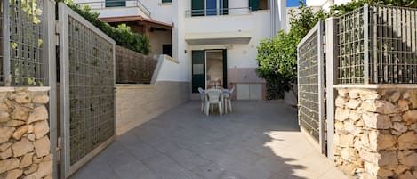 Un patio con pared de piedra, puerta metálica y una mesa con sillas.