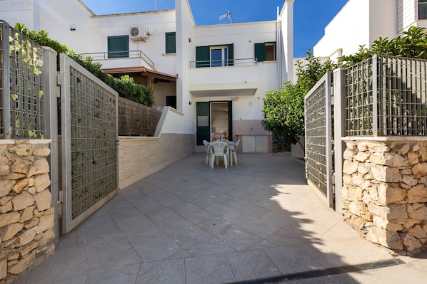A courtyard with a stone wall, a metal gate, and a table with chairs.