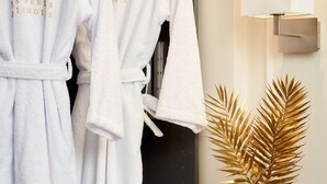 Two white robes with gold text hanging on a wall, a gold decorative plant, and a modern light fixture. - Blackpearl-HyperKing Bed CenterSize-Parking Offered (Amiens)