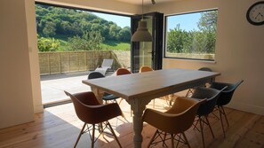 A dining area with a table and chairs, large windows with a view of greenery, and a clock on the wall. - Echium Heights, 4 bed retreat, secluded with views (Ilfracombe)