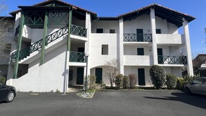 Ein mehrgeschossiges Gebäude mit weißer Fassade, grünen Geländern und einem Parkplatz.