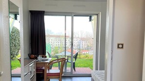 Ein Zimmer mit einem Bett, einem Schreibtisch mit Stuhl und Blick auf einen Garten sowie Gebäude durch eine Schiebetür.