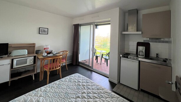 Ein gemütliches Hotelzimmer mit Bett, Küchenzeile, Essbereich mit Tisch und Stühlen, Fernseher und großem Fenster mit Blick ins Freie.