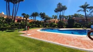 A swimming pool surrounded by palm trees and a brick walkway.