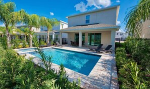 Relax by the spacious outdoor pool surrounded by lush greenery and enjoy the patio area with comfortable seating.