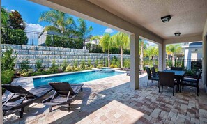 Un espace extérieur abrité comprenant une piscine, des chaises longues et une table avec des chaises.