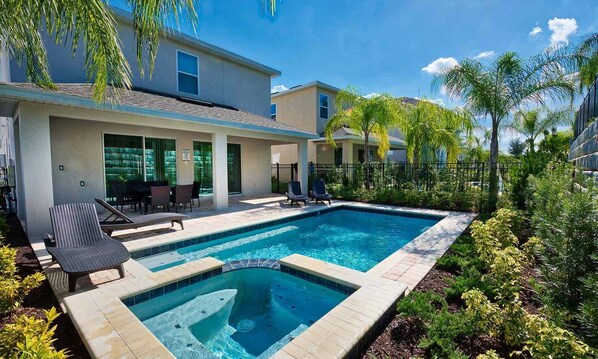 Relax by the pool with a hot tub and outdoor seating on the covered patio surrounded by lush landscaping.