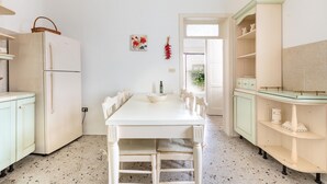 A kitchen with a white table, a refrigerator, and a cabinet with shelves. - 2068 Villa Marina Salentina (Porto Cesareo)