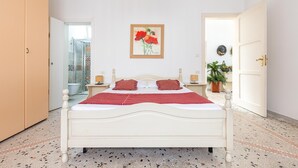 A bedroom with a white bed, red pillows, a framed painting, a potted plant, and a door leading to a bathroom. - 2068 Villa Marina Salentina (Porto Cesareo)