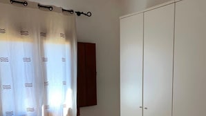 Un dormitorio con cama, armario, ventana con cortinas y radiador.