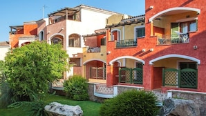 Un edificio residencial de varios pisos con balcones, puertas de arco y un jardín bien cuidado.