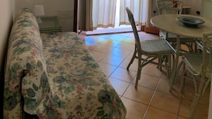 Una habitación con un sofá floral, una mesa de comedor con sillas y una ventana con cortinas.