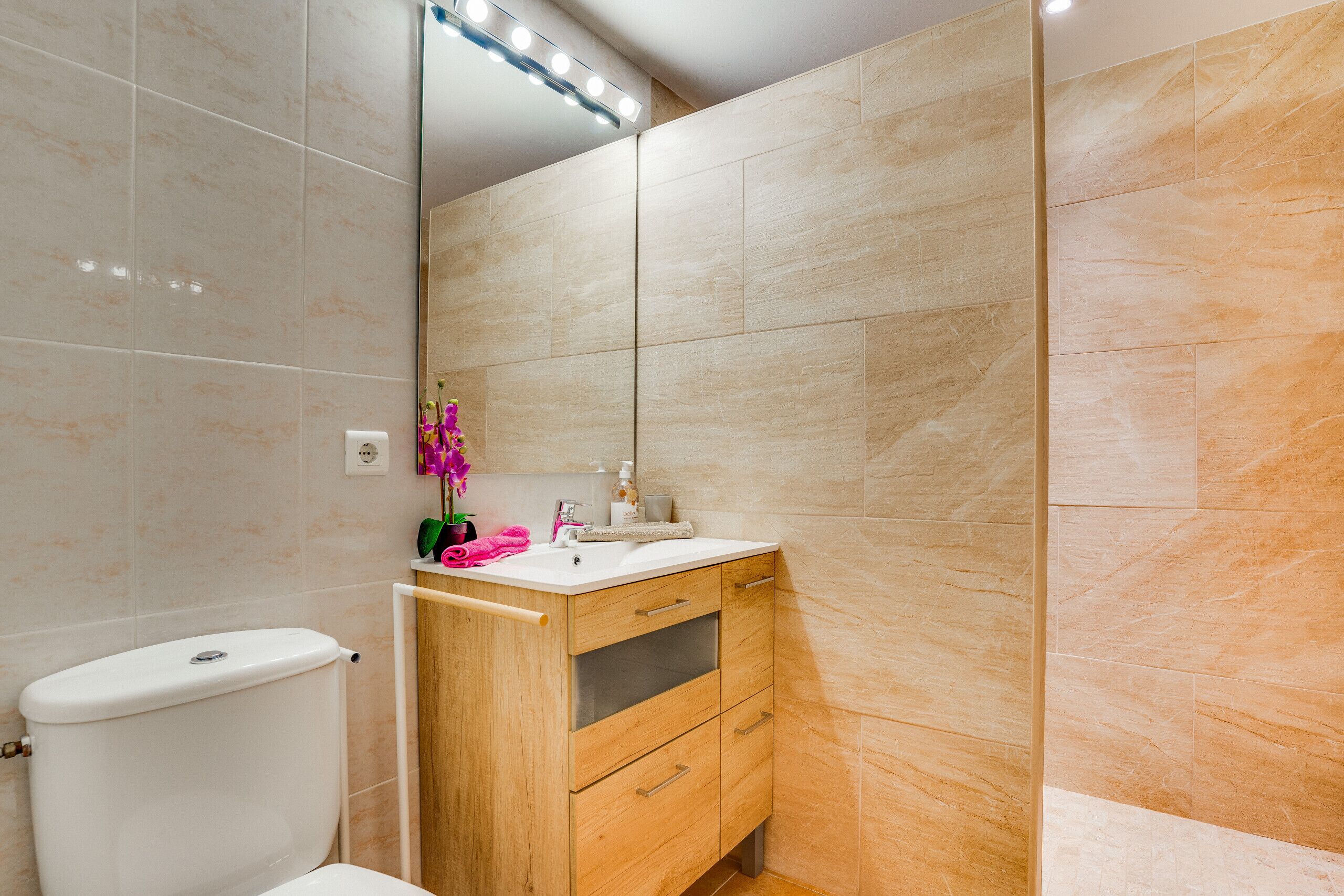 A bathroom with a toilet, a wooden vanity with a mirror, and beige tiled walls.