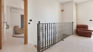 Un vaste espace de vie au design moderne, doté d’un plafond haut, d’une rampe décorative et d’un coin salon confortable avec un canapé et un fauteuil.